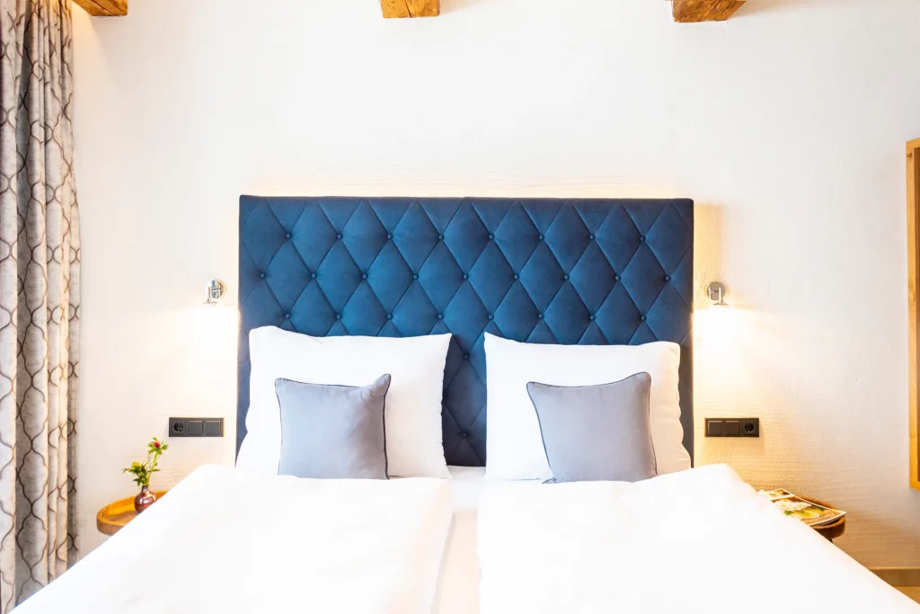 Elegantes Doppelbett mit gestepptem blauem Kopfteil und weichen Kissen im Ferienhaus Mandlberggut in Radstadt/Mandling.
